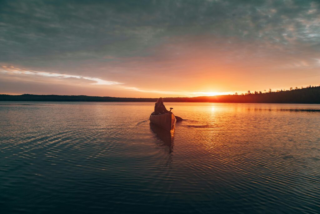 A lone canoeist paddling on Ely Lake at sunset, capturing nature's serene beauty.